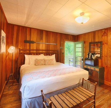 front view image of a cozy double bed in a room with wooden walls and flooring with a small chandelier - Historic Tapoco Lodge
