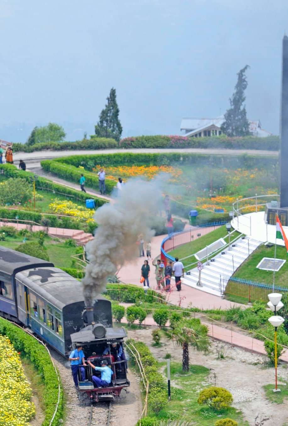 Toy train passing through Batasia Loop garden, with manicured lawns and mountain views.