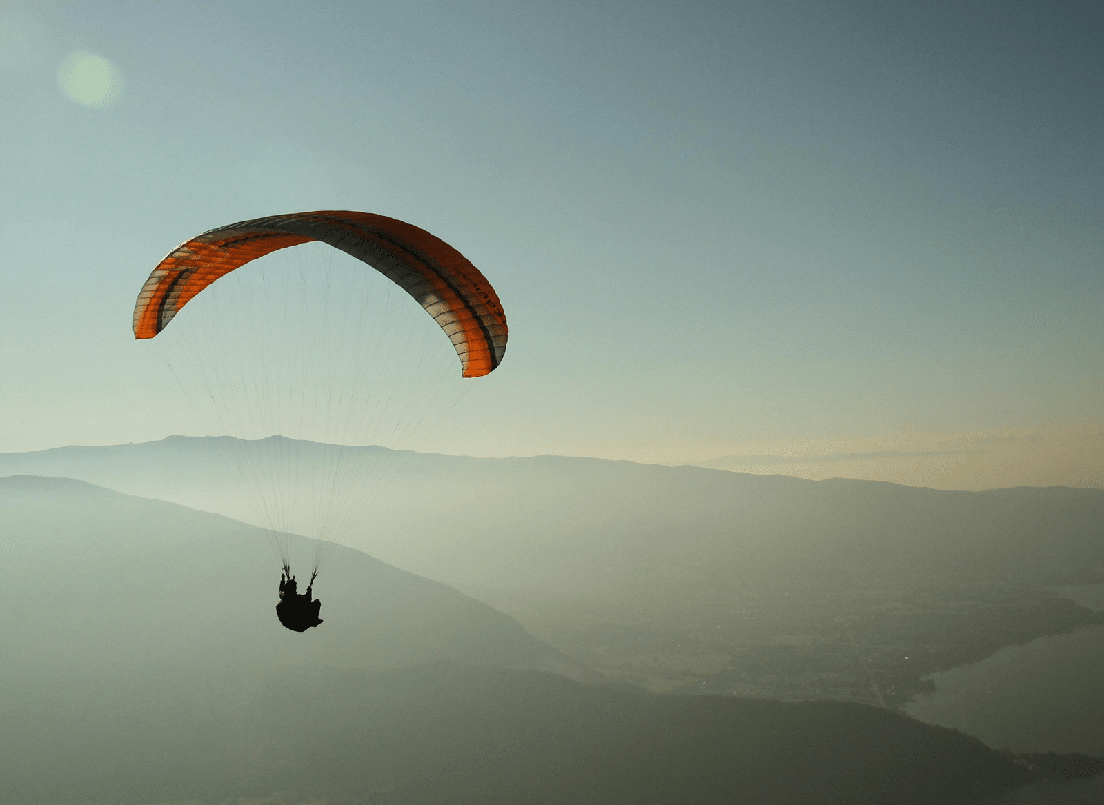A man in a parachute amidst mountains in the sky.