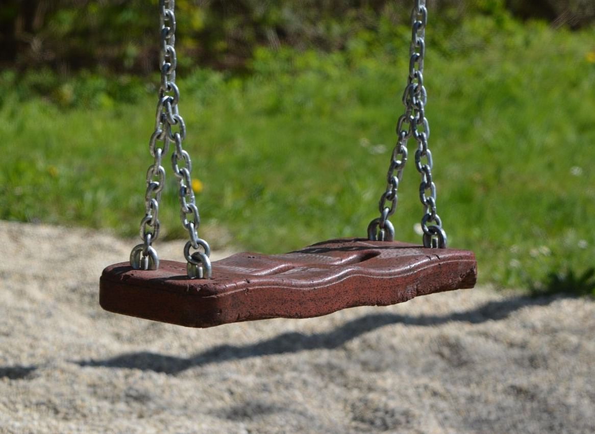 A swing hanging above a sand pit adjacent to a lawn space.