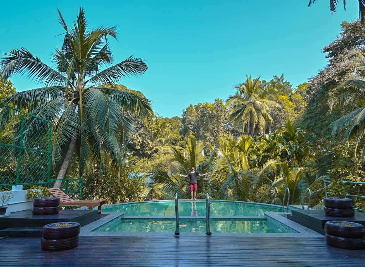 A serene outdoor swimming pool nestled amongst dense tropical foliage and palm trees under a clear blue sky - Sea Hills Hotels, Sri Vijaya Puram (Port Blair)