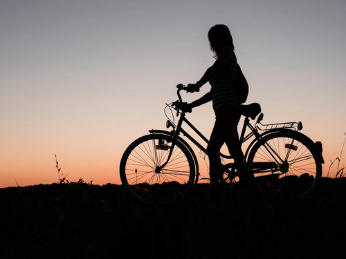 the silhouette of a woman with her cycle in the evening