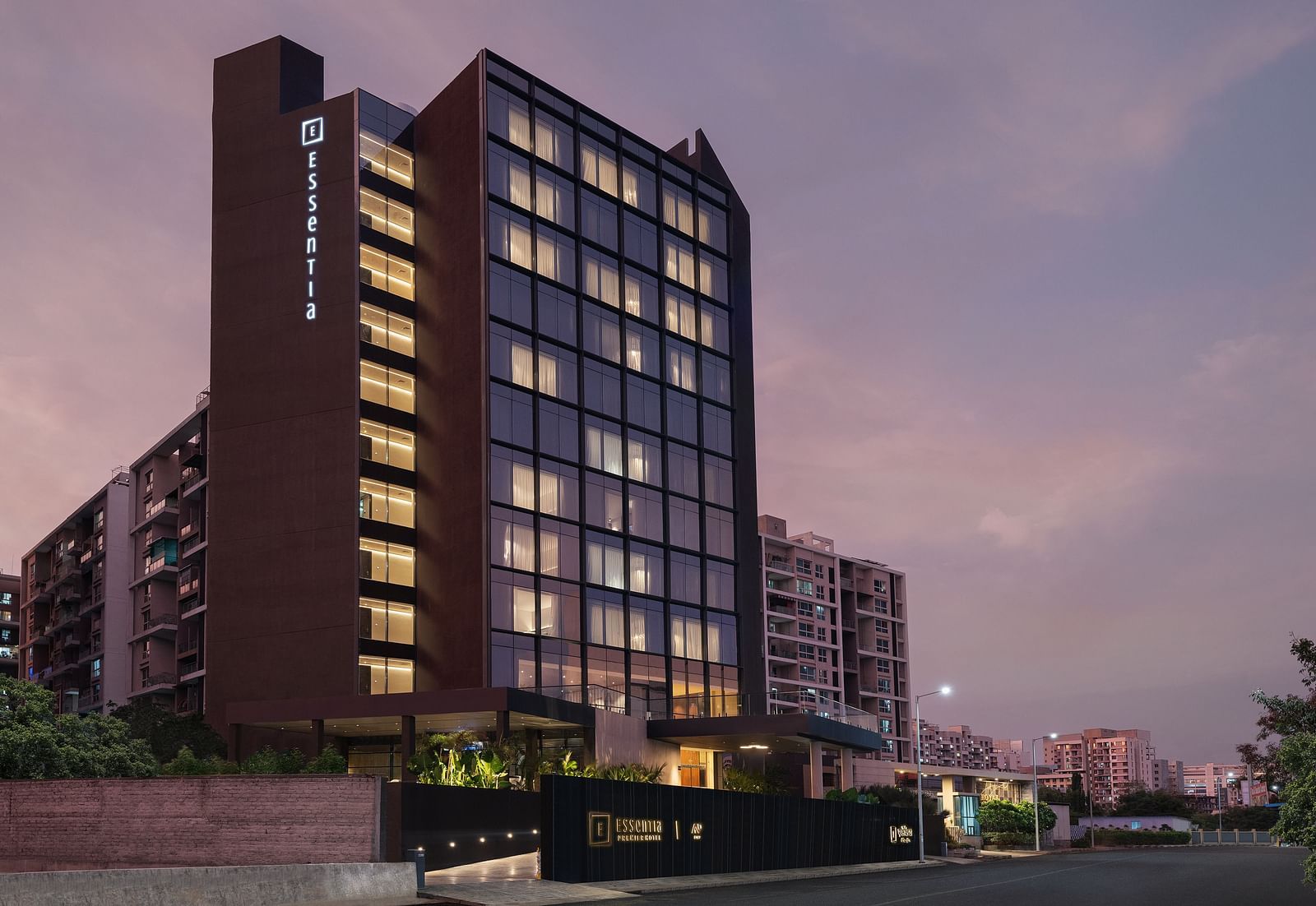 Facade of Essentia Premiere, Pune with lights on during twilight.