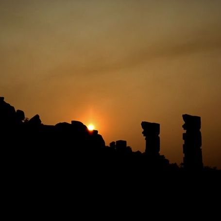 Silhouetted Hampi temple ruins at sunset.