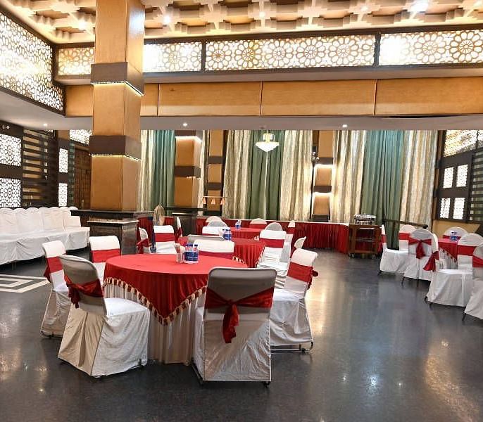 A beautiful conference hall with elegant lights in the ceiling featuring round tables set up all across the hall at Hotel Gold, Panipat.