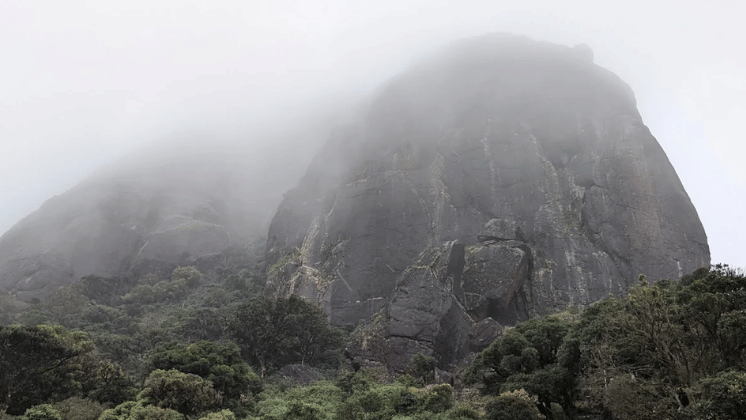 Rocky mountain peak partially hidden by thick fog and low clouds.