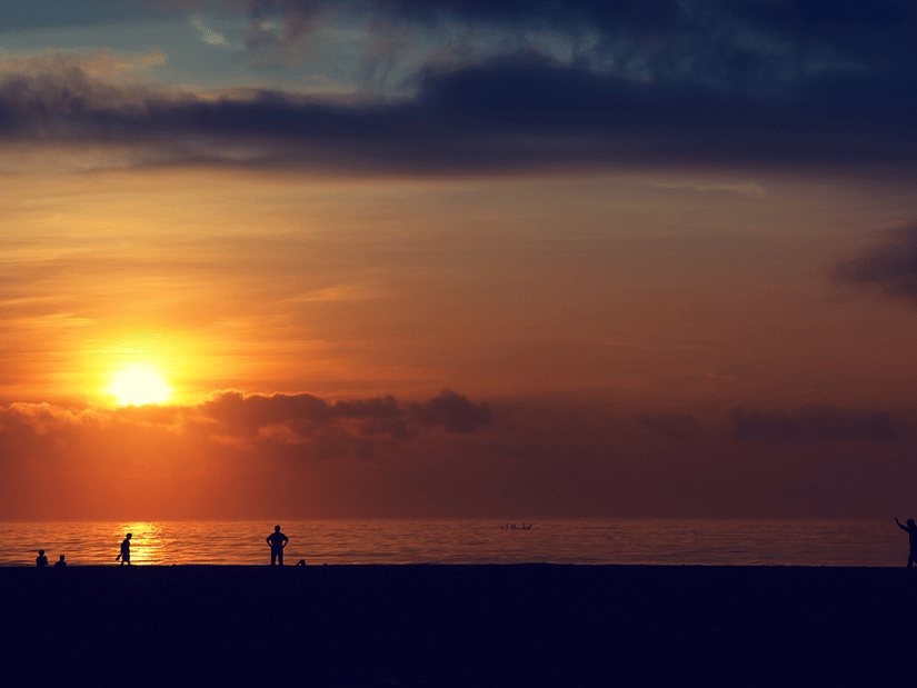 Sun setting in the distance at Marina Beach in Chennai with people walking on the beach side.