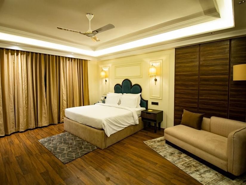Side view of luxury villa room with a cozy, spacious bed and a sofa in the corner at Wedlock Greens Hotel & Resort, Dhanbad