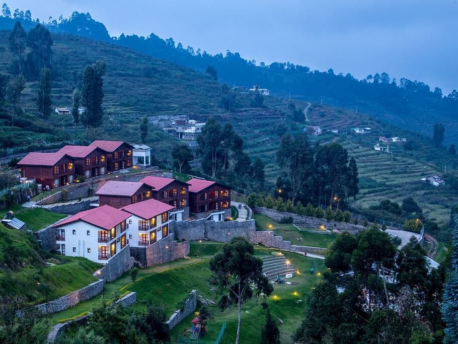 A drone shot of the GReaT Trails Kodaikanal By GRT Hotels property surrounded by lush greenery and trees with a clear sky