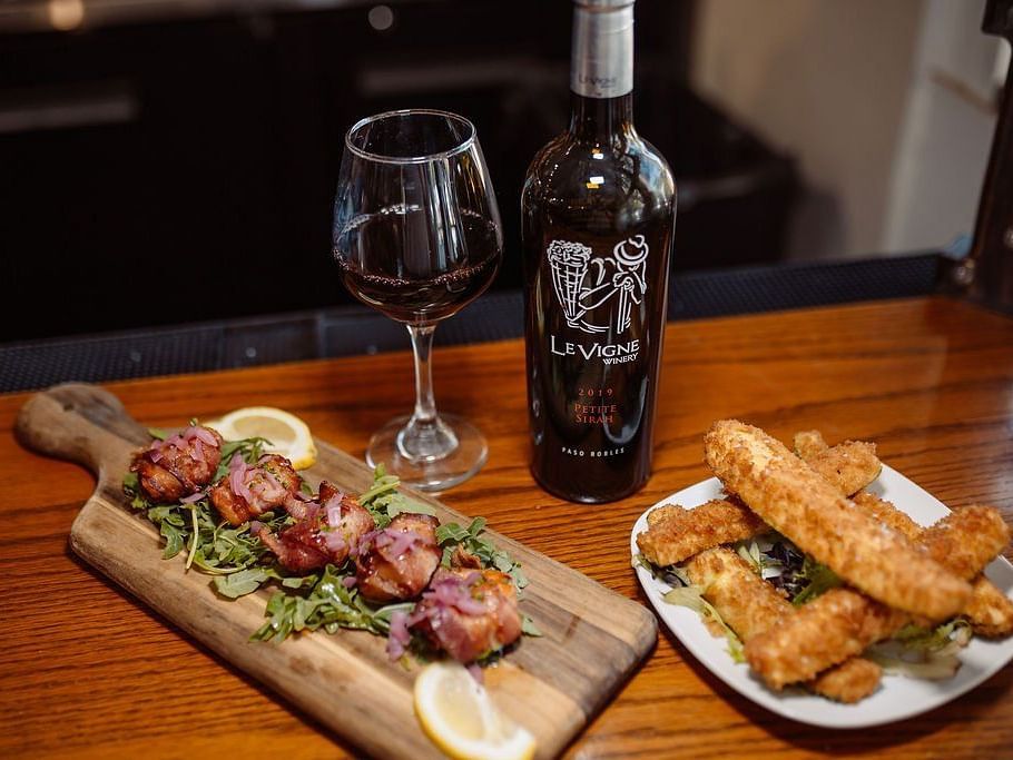 Two dishes being served alongside a bottle of red wine on a wooden table - Narrow Gauge Inn - A Serenite Hotel Near Fish Camp.
