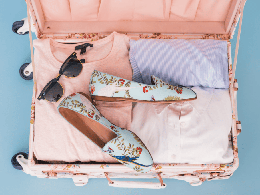 A pink suitcase is open, revealing neatly packed clothes and accessories.