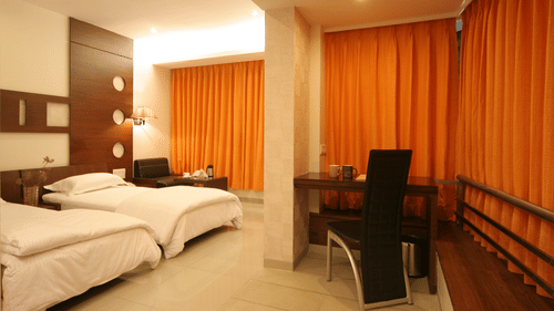 Well-lit Executive Rooms in Pride Biznotel Alkapuri featuring plush beds and a work desk at a distance
