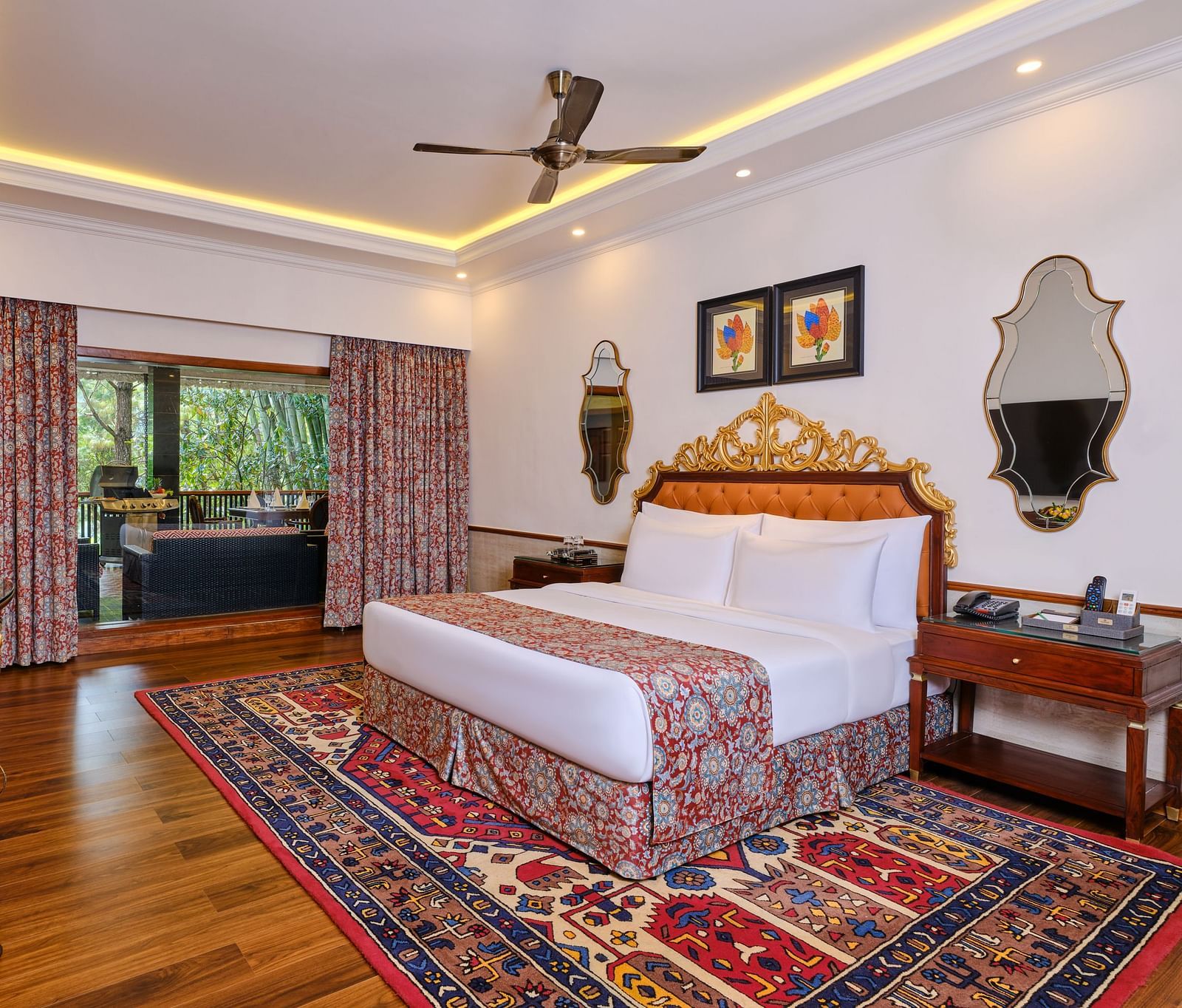 a luxurious regent villa, where a table and a grand bed sits beneath a decorative headboard and artwork on the wall with two mirrors. 