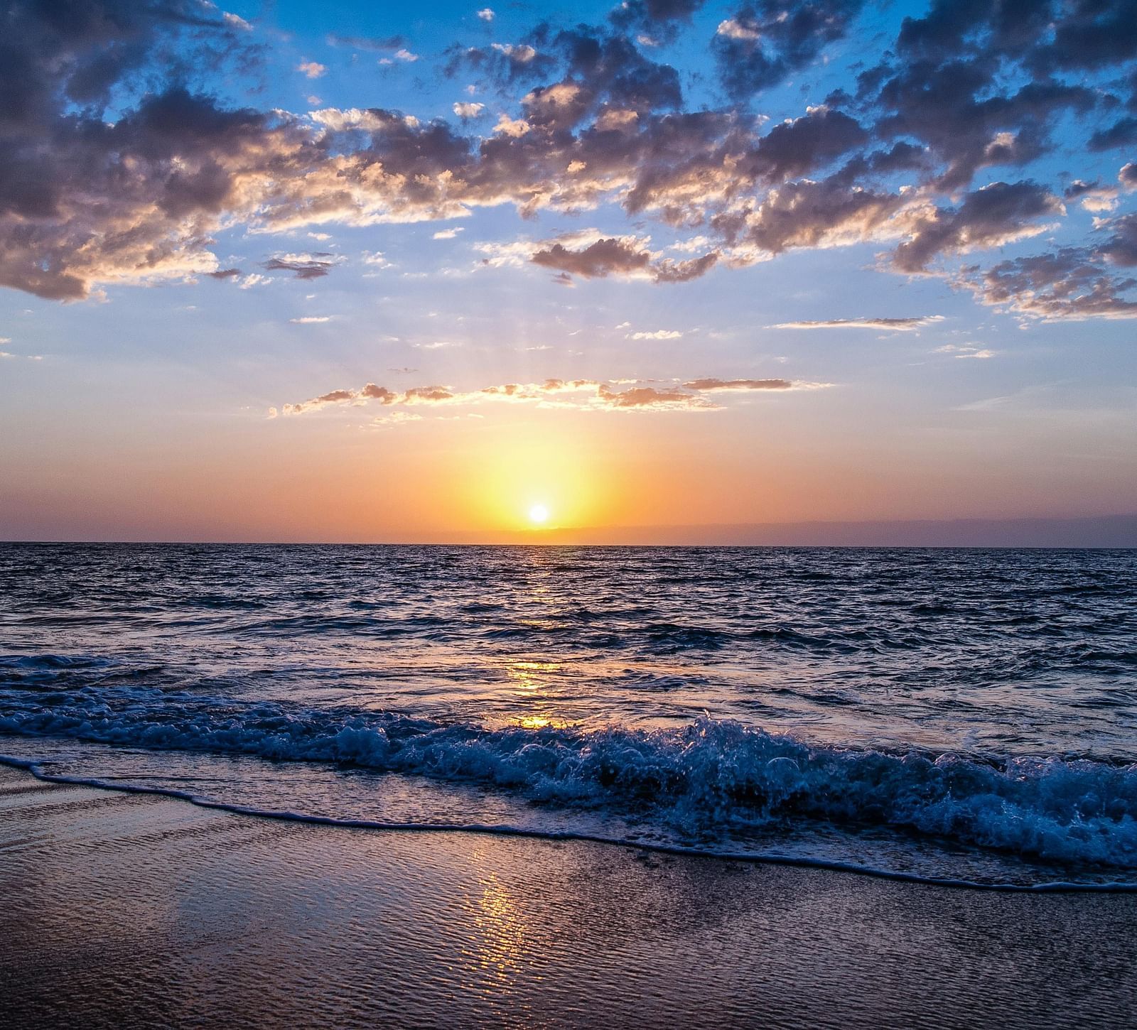  A sunrise view from the beach shore, with the sun reflecting on the water and a cloudy sky overhead