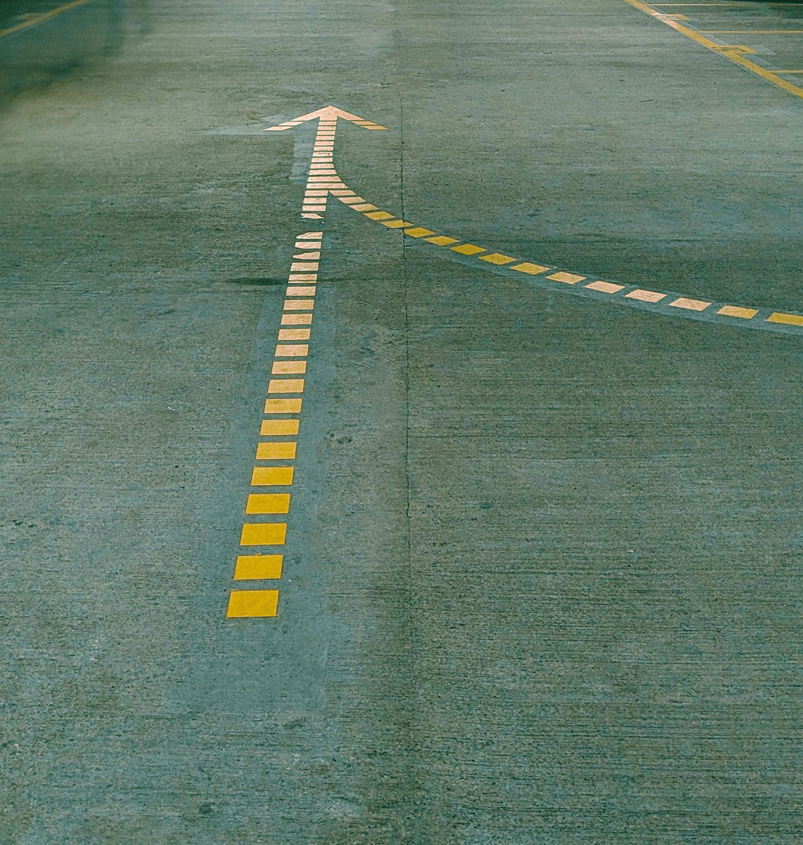 A low-light underground car park with yellow painted lines and a single white arrow on the concrete floor.