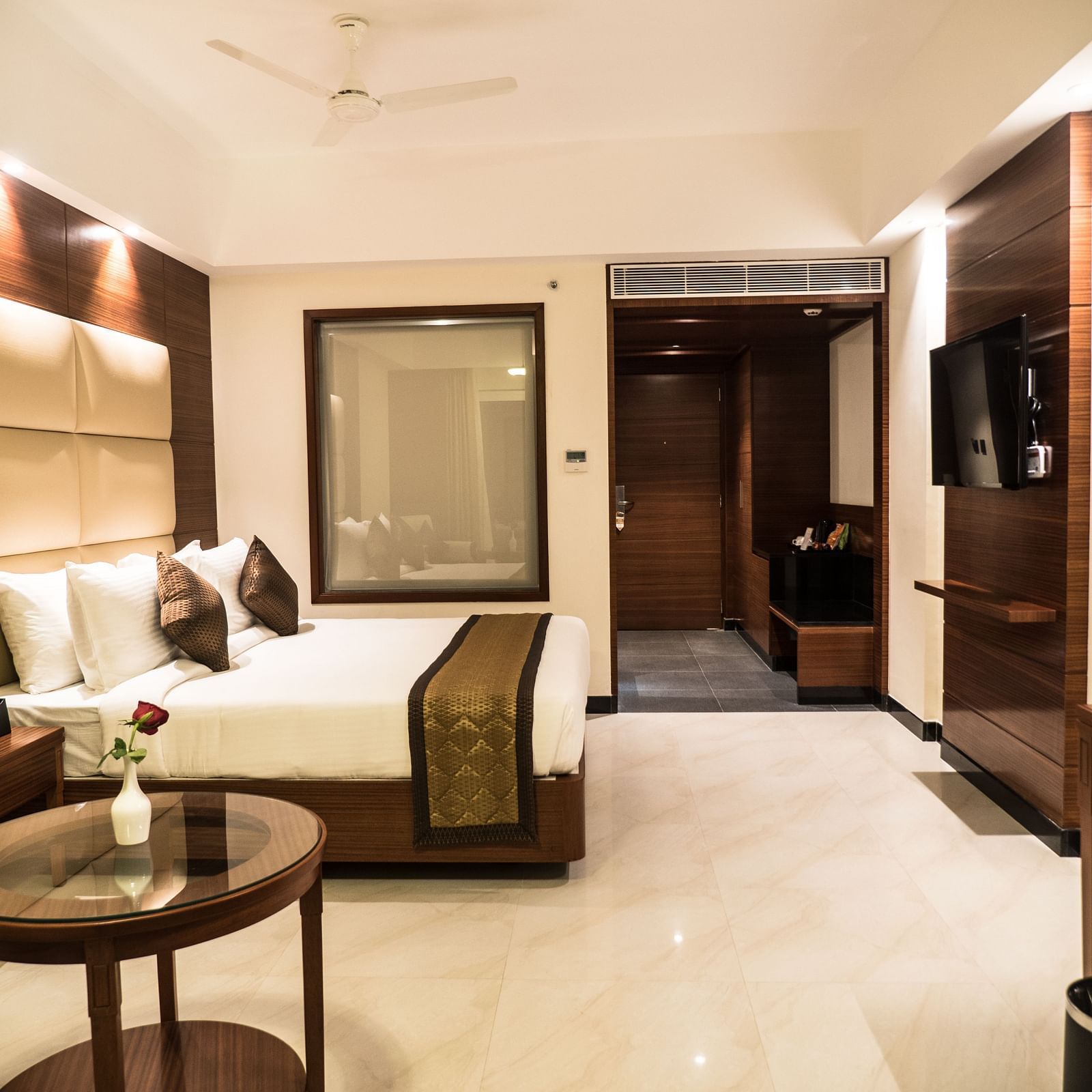 Side angle view of a Premium Room showcasing a bed, tea table, flat-screen TV, wall frame, and warm lighting.