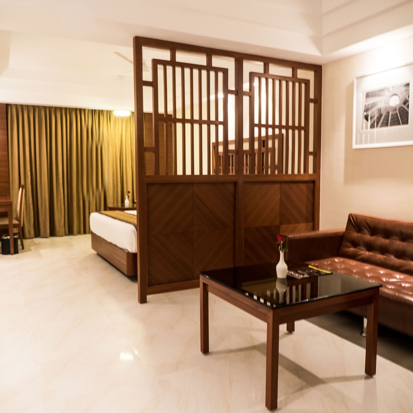 Interior view of a Premium Suite featuring a corner layout. A divider separates the living area with a sofa and tea table from the bedroom area, which includes a bed and a flat-screen TV at MM Legacy.
