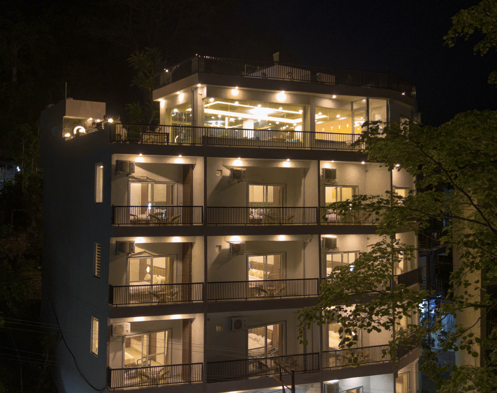 A multi-storey building exterior at night, with windows lit up and trees surrounding the structure in Perfectstayz Premium Mystic Falls, Rishikesh.