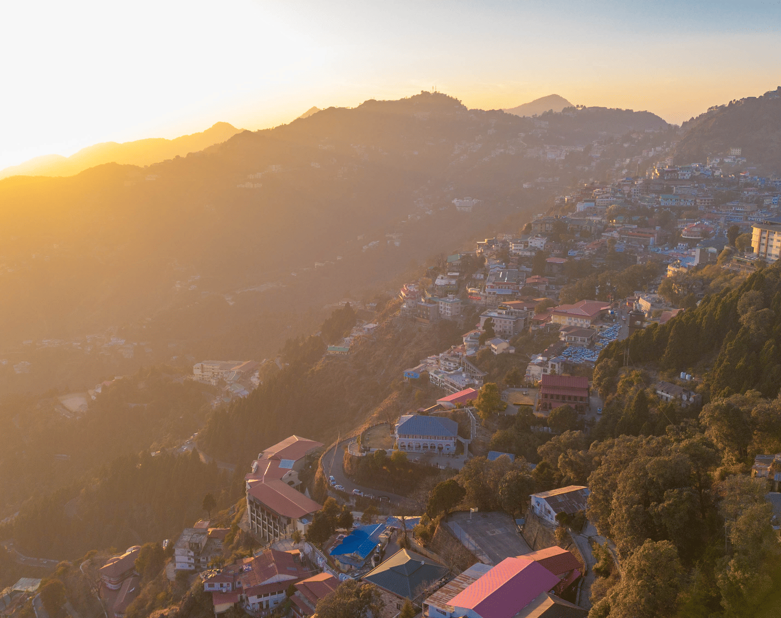 A panoramic view of a mountain town built on rolling hills, bathed in the golden light of sunrise or sunset | Perfectstayz Value Valley Vista