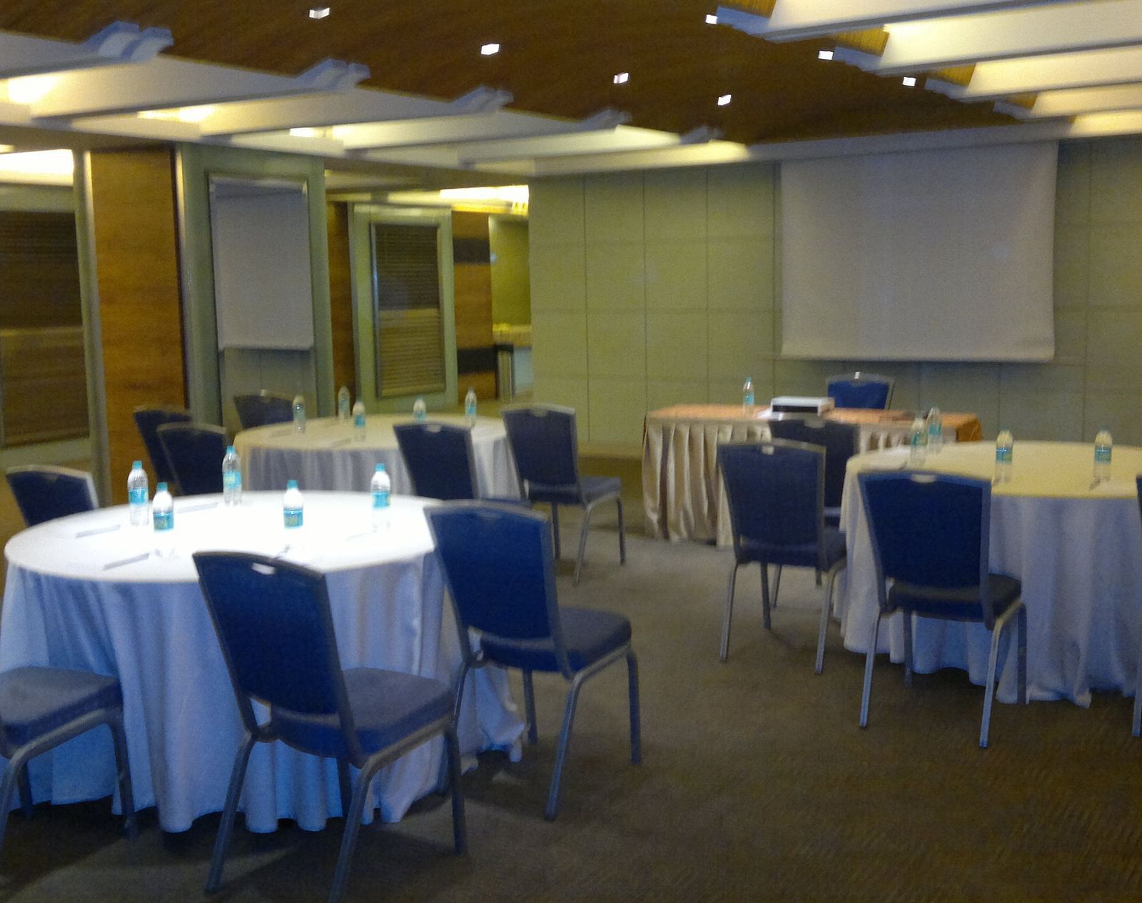 Image of an event space at Mirage Hotel featuring round tables and blue chairs along with a white board | Mirage Hotel