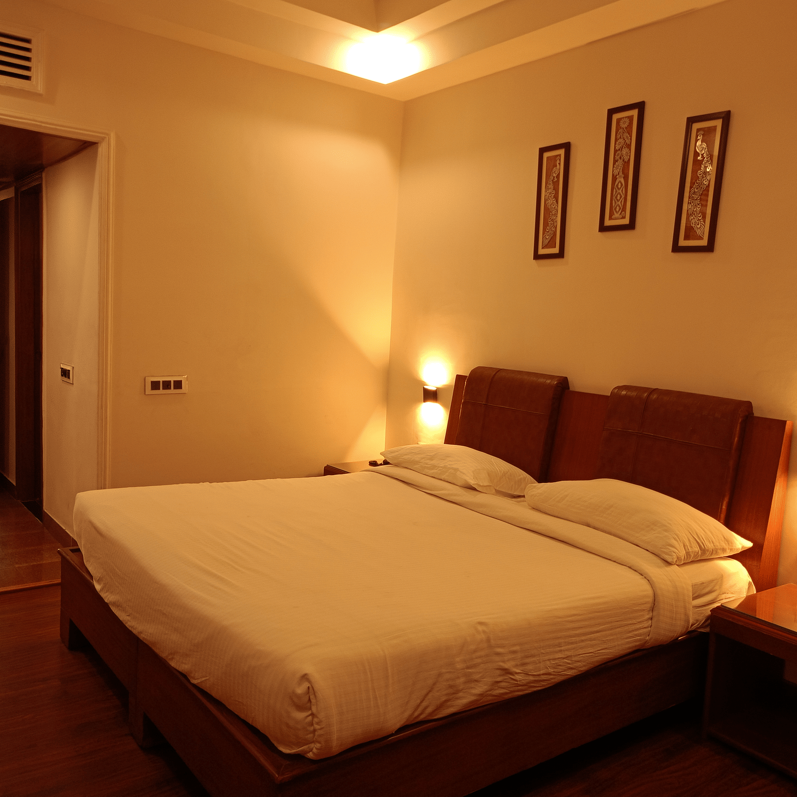 Guest room at Hotel Gold, Panipat featuring a bed, side tables, and framed wall art.