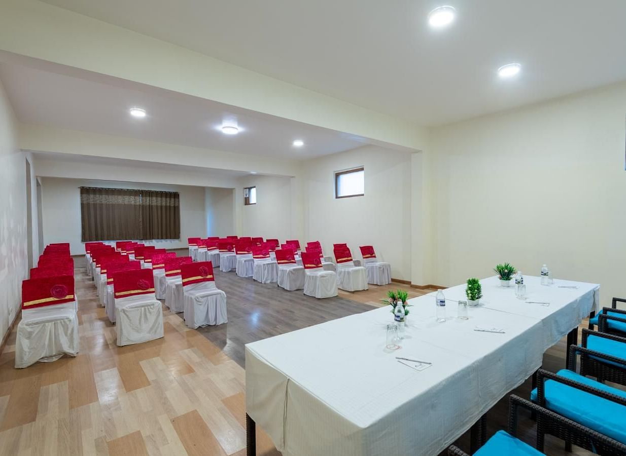 The image shows a conference room with several rows of red chairs, and a long table with blue chairs | DLS Serenity Resort and Spa