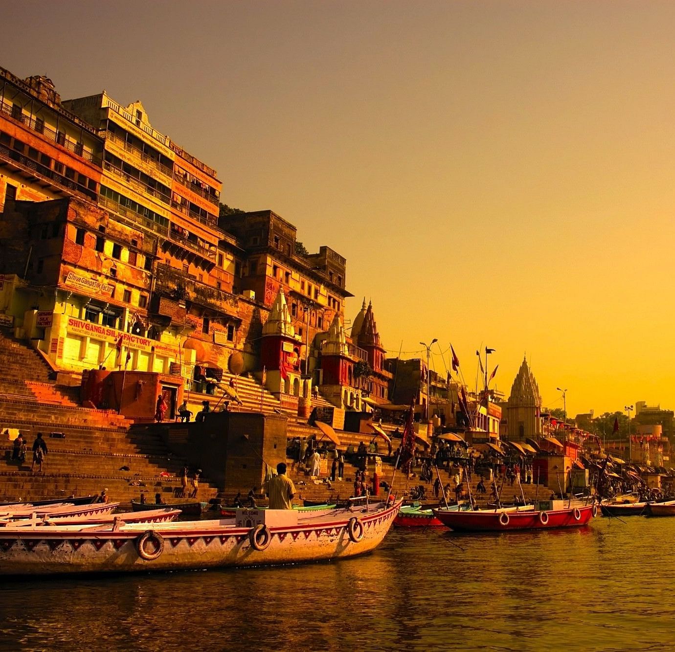 Sunset view of a city, featuring a lake with boats on it and a line of buildings.
