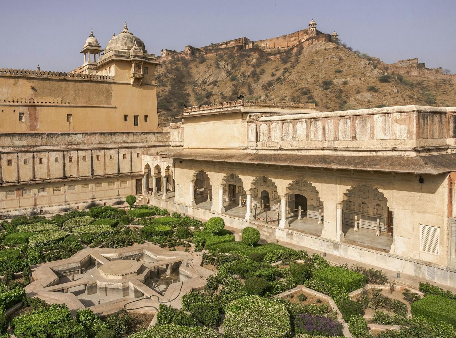 A scenic view of Amber Fort in Jaipur, Rajasthan, showcases its intricate architecture, a formal garden with water features, and the surrounding hills.