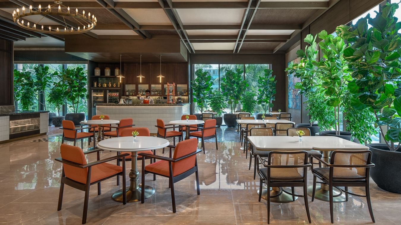 Wide-angle view of the dining area at The Residency Towers Chennai, featuring glass windows and lush greenery outside.