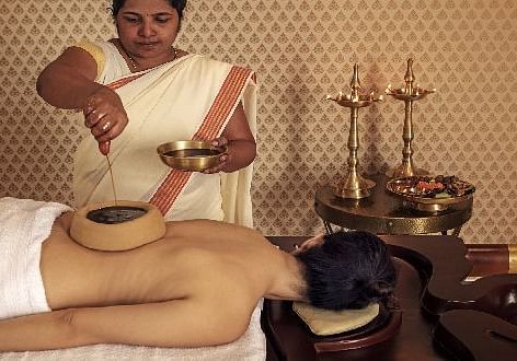 A therapist applying warm herbal oil to a client's back using traditional Ayurvedic techniques - Shreyas Retreat
