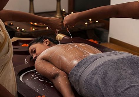 A therapist pouring warm herbal oil on a client’s back during an Ayurvedic treatment - Shreyas Retreat