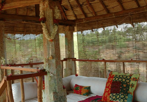 A covered outdoor patio with seating and a wooden railing, natural light - Shreyas Retreat