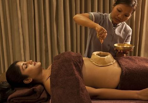 A therapist pouring liquid on a client's stomach during an Ayurvedic treatment - Shreyas Retreat