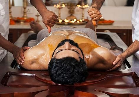 A person receiving a massage on a wooden table, with hands applying treatment - Shreyas Retreat