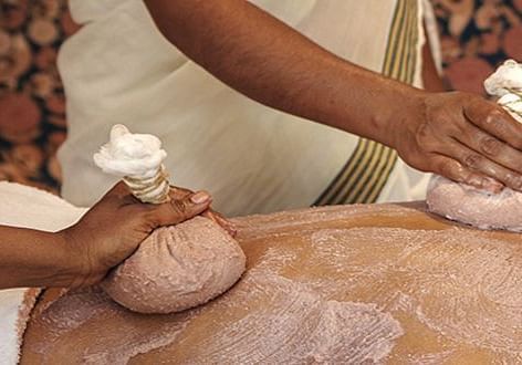 A close-up of hands applying an Ayurvedic herbal scrub to a client's body - Shreyas Retreat