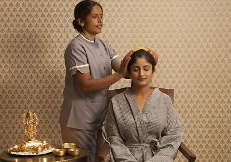 Two people in robes, one seated, indoor setting, spa treatment - Shreyas Retreat