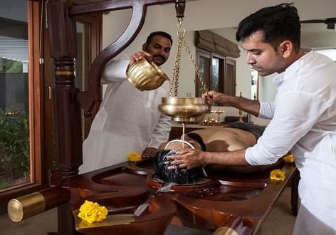 A therapist pouring warm herbal oil on a client’s back during an Ayurvedic treatment - Shreyas Retreat