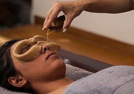 A close-up of a person receiving a treatment on their face, wooden table - Shreyas Retreat
