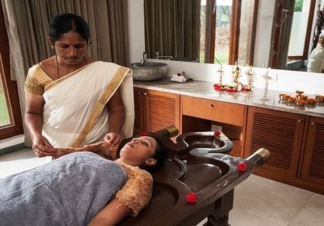A person receiving a massage on a table, with another person standing nearby, indoor setting - Shreyas Retreat