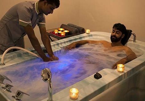 A person receiving a massage on a lit-up table, with another person standing - Shreyas Retreat