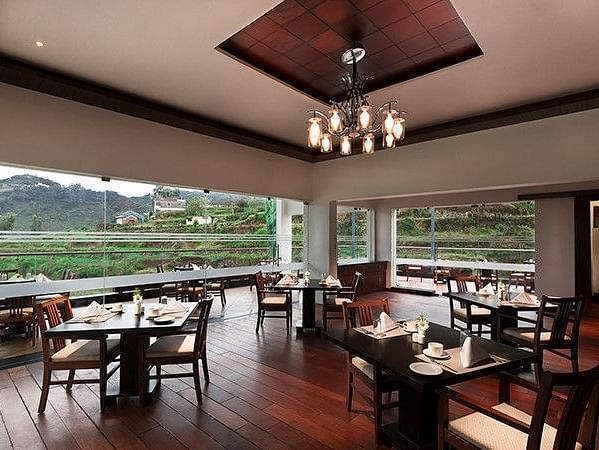 Shot of a restaurant full of tables, chandelier and a big window with mountain in the background.
