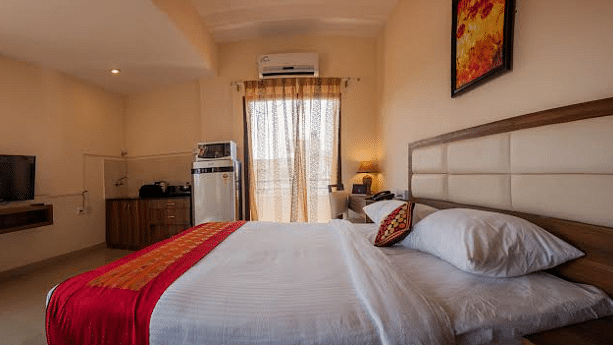 A hotel room with a neatly made bed, television, and partially visible window | Astra Hotels and Suites Electronic City