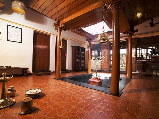 A traditional-style interior at Ayur Ashram, Uday Samudra Leisure Beach Hotel featuring wooden pillars, terracotta flooring, and brass decor accents