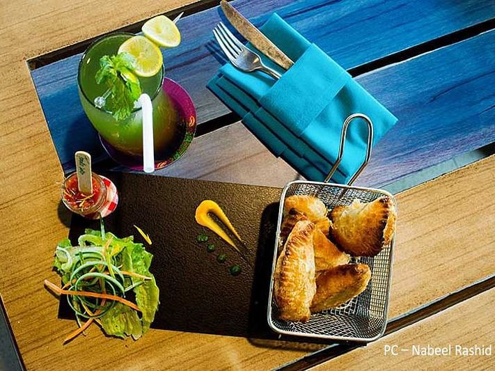 Fried snack served with a side salad and a drink along with cutlery wrapped in a blue napkin.