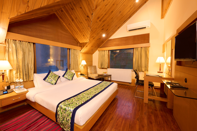Renest Manali - interior view of the Hornbill bedroom featuring a king size bed with green throw pillows and bed scarf