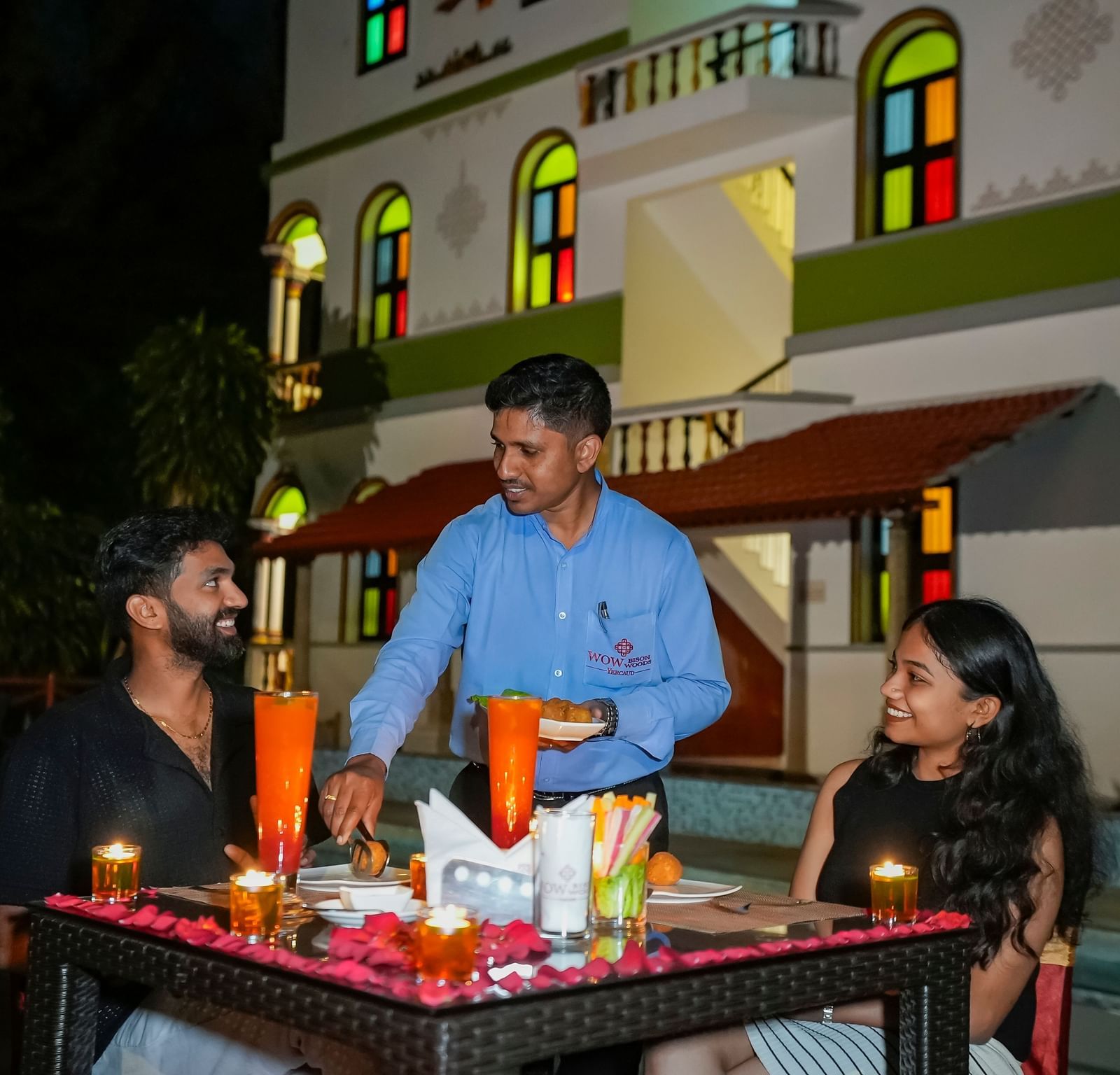 A couple having a meal outdoors with a waiter serving them.
