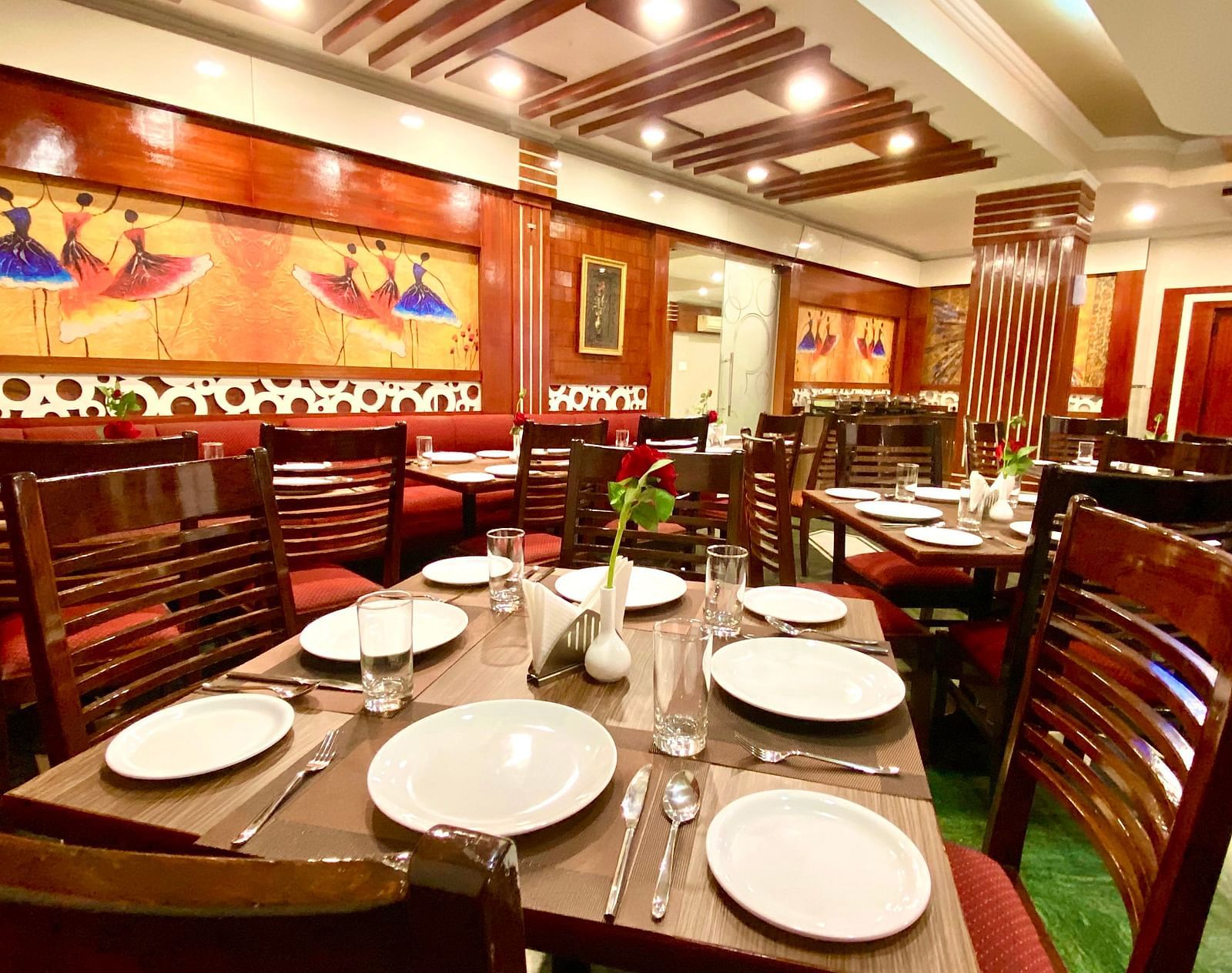 Dining area at DLS Park Grace, Haridwar featuring wooden chairs, ceramic plates, wall art and false ceiling.