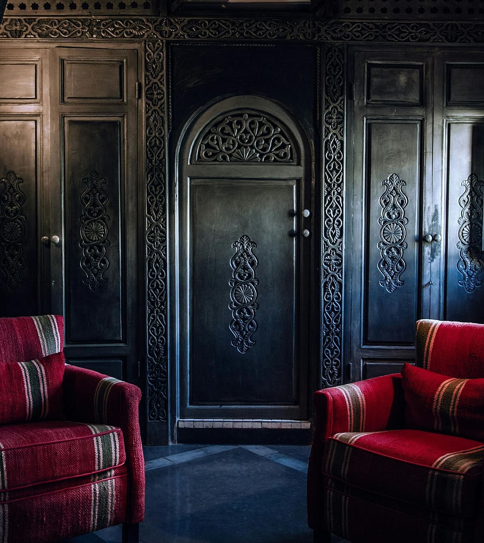 A room with red sofas and wood carved door and panels.