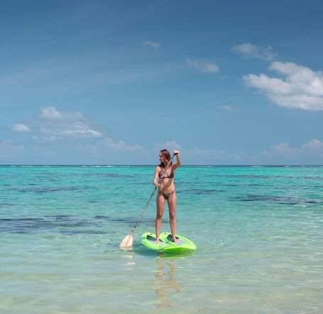 A woman balancing on a stand-up paddleboard in shallow turquoise water, moving forward while using a long paddle | Abaco Inn
