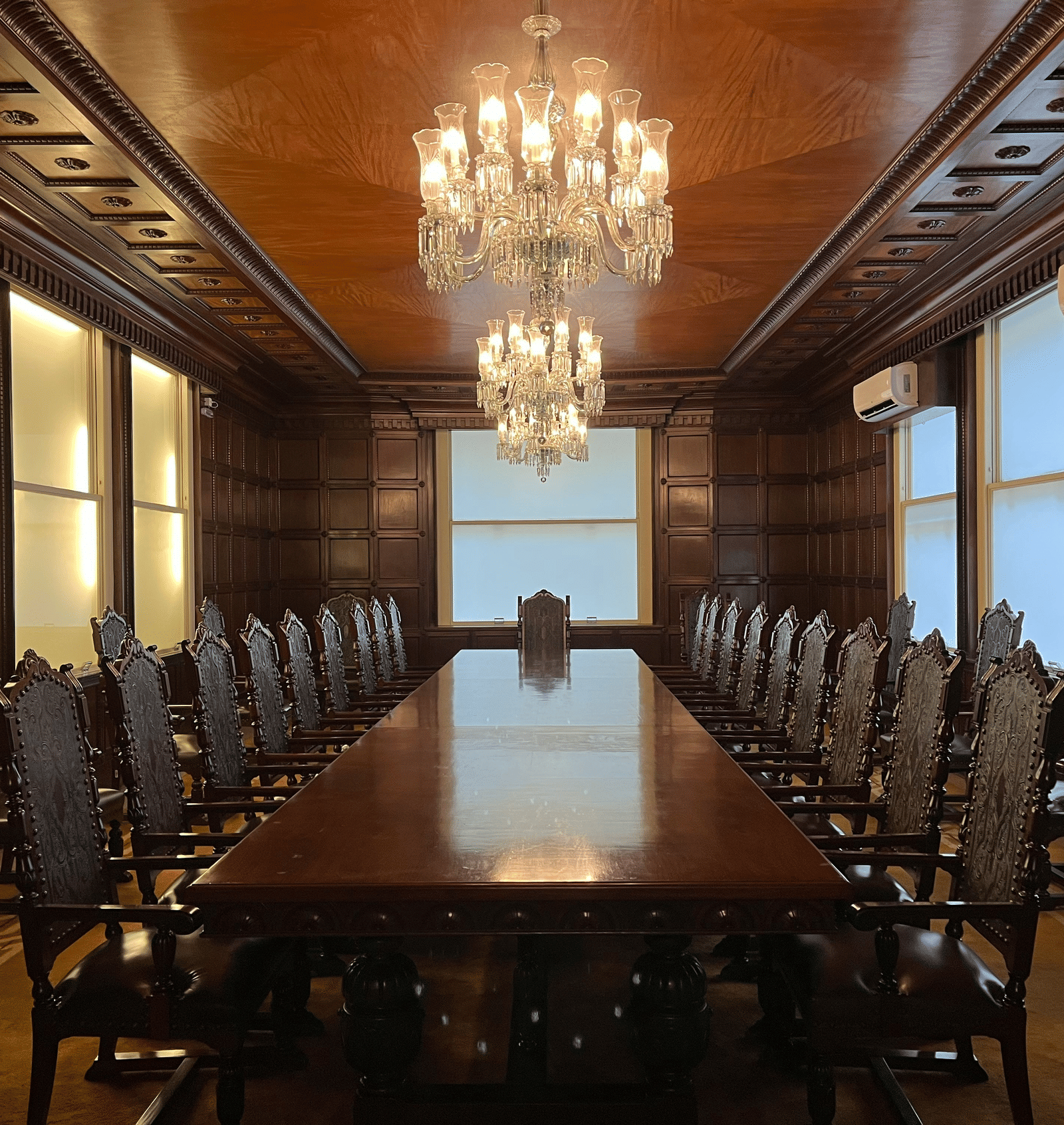 Traditional, luxurious boardroom with dark wooden panelling, a long mahogany table, and crystal chandeliers.